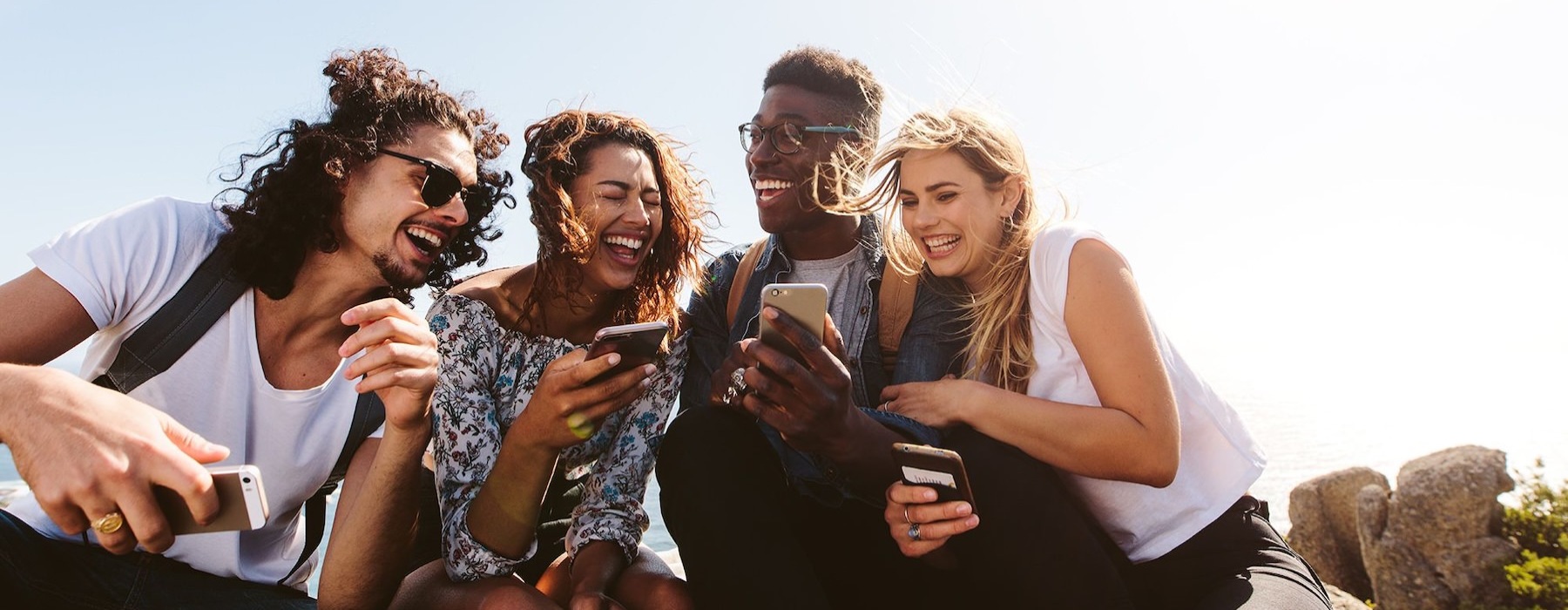 a group of friends sit outside laughing over their cell phones